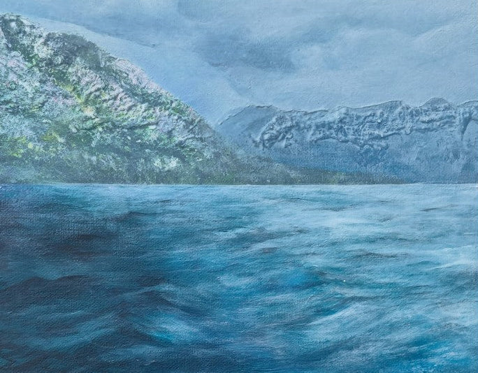 A landscape painting depicting a vast, textured blue sea in the foreground with rugged mountains covered in patches of snow under a cloudy, overcast sky.